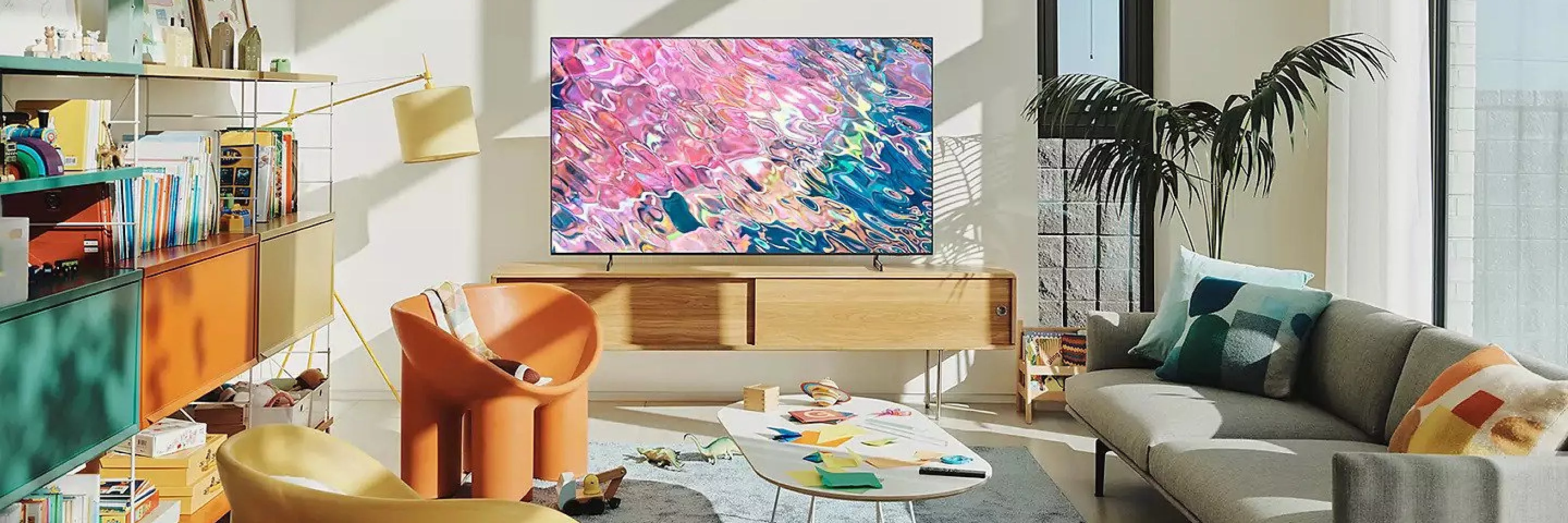 Modern living room with smart TV showing colourful abstract art, wooden media unit, sofa and indoor plant.