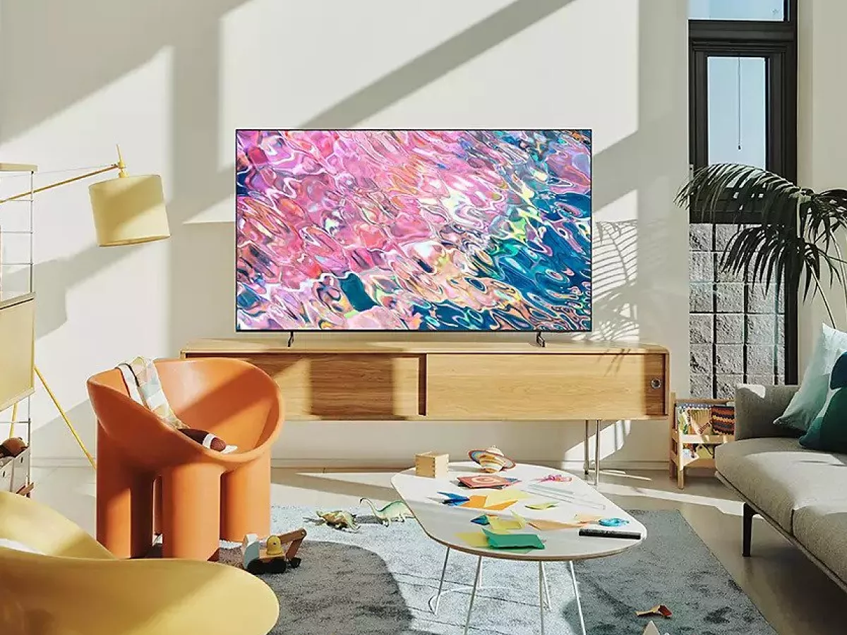 Modern living room with smart TV on wooden console, colourful abstract screen, sofa, bookshelves and plants.