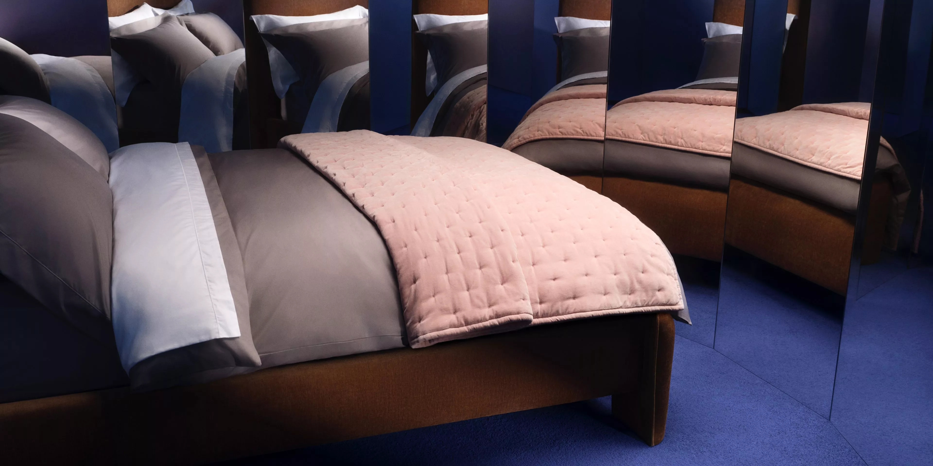 Bed with bedding and pillow, next to lots of mirrors