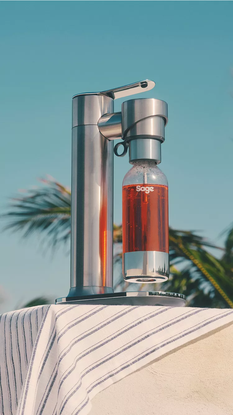 An InFizz Fusion Sparkling Drinks Maker, in Black, with blue skies and palm trees in the background