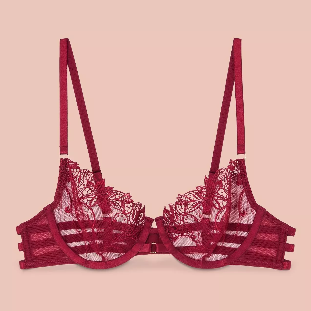 Elegant red lace bra with intricate floral embroidery and adjustable straps, set against a soft peach background.