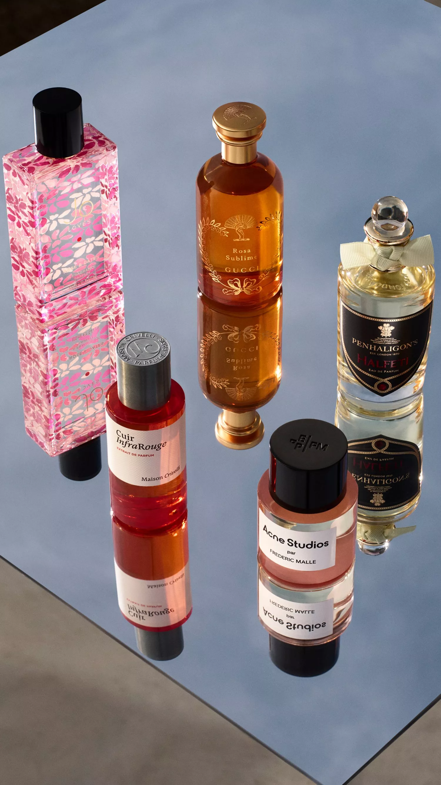 A stylish display of five perfume bottles on a reflective surface, showcasing elegant designs and labels.