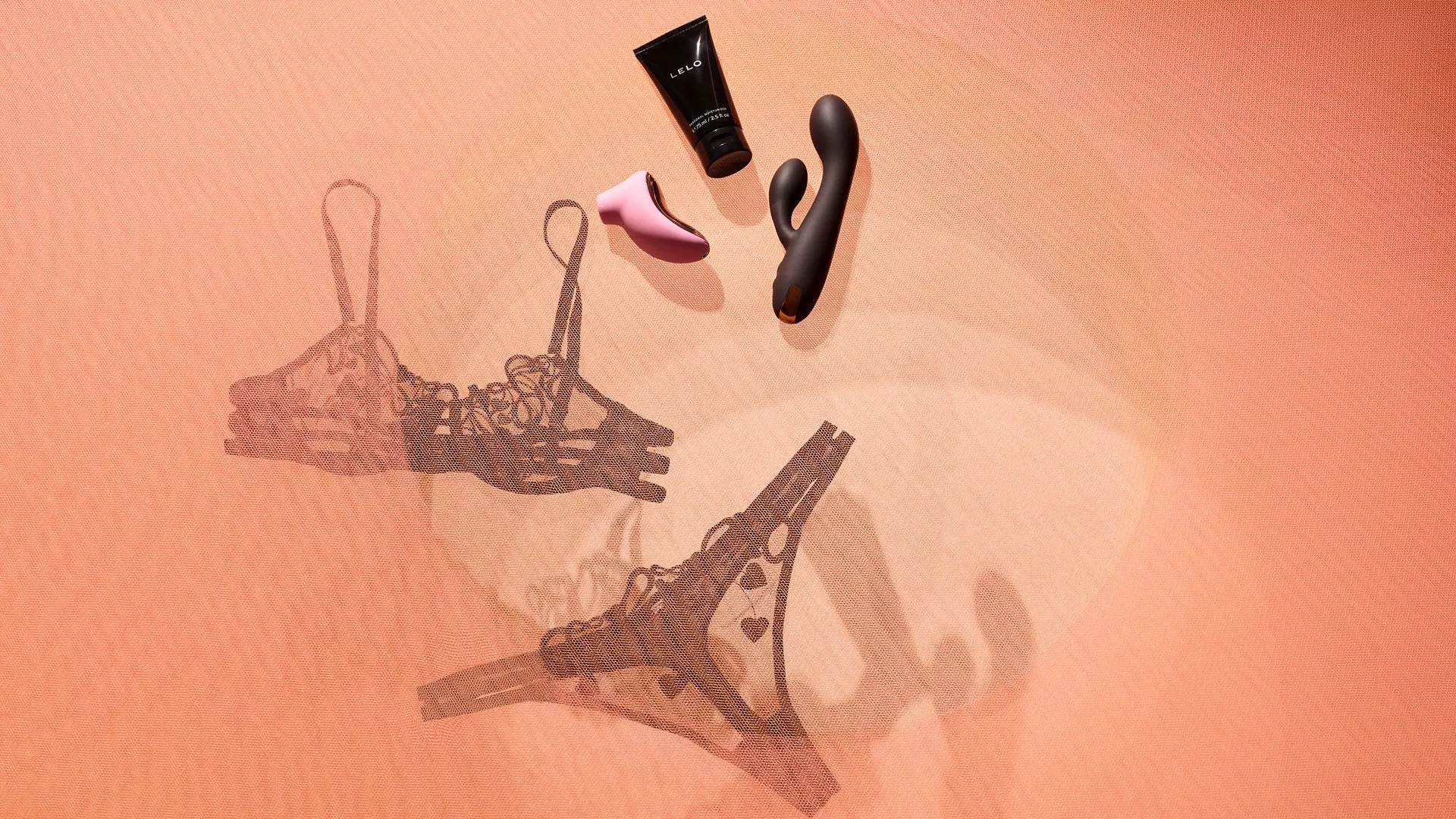 Lace lingerie set with black tube, pink and black toys on peach fabric, creating a sensual aesthetic.