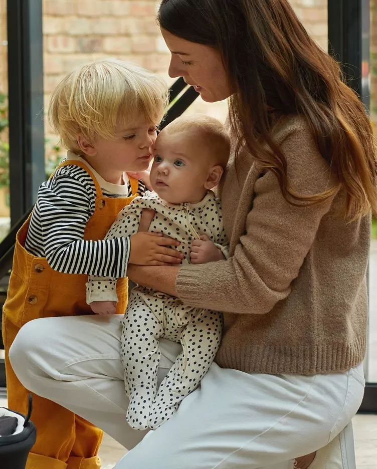 a mother holds a small baby whilst a toddler cuddles
