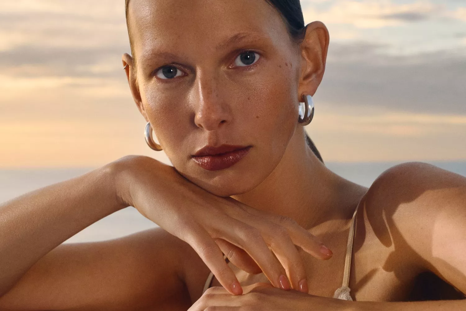 Close-up portrait of a woman wearing silver hoop earrings at sunset, showcasing natural beauty and skincare glow