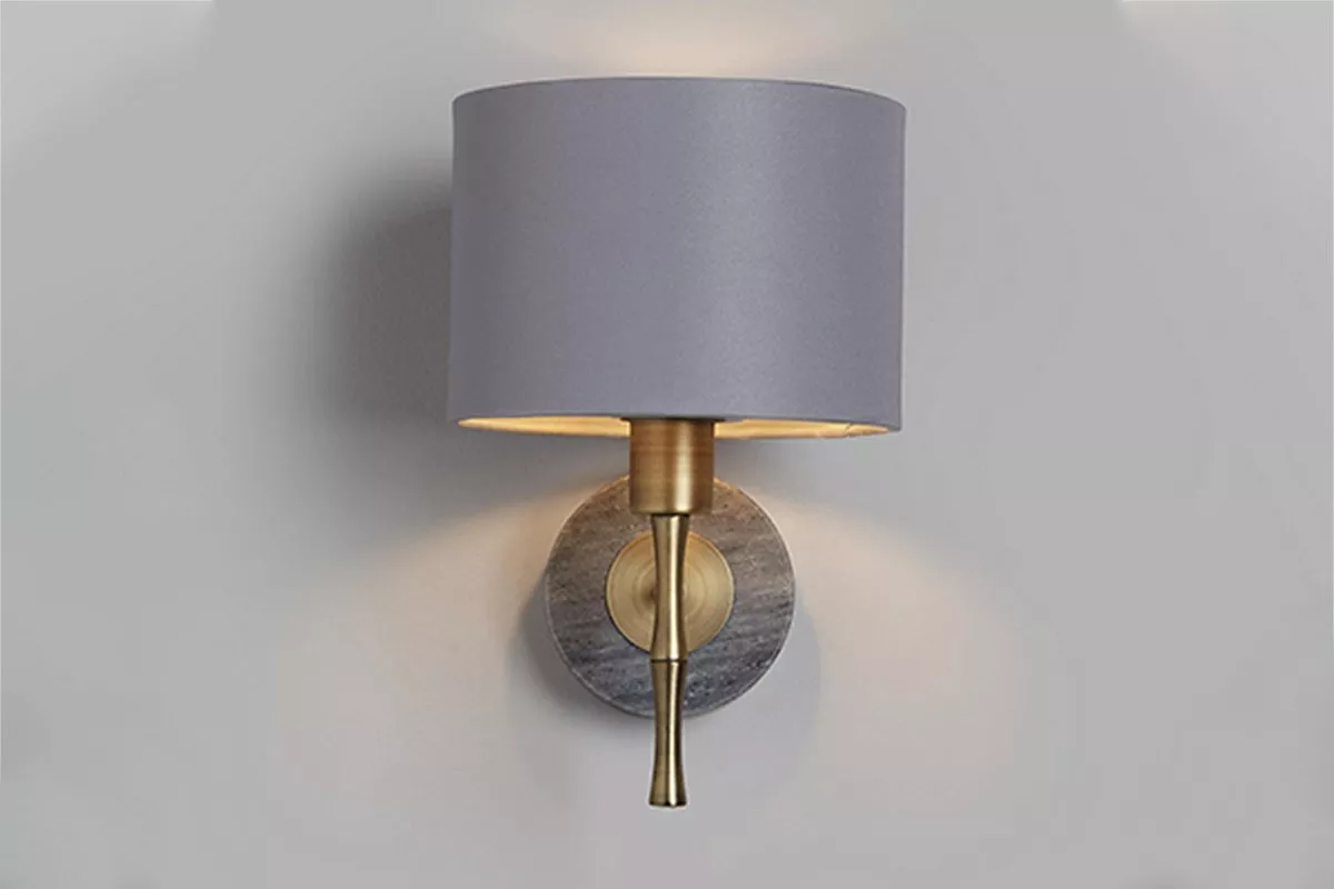 Modern wall sconce with grey fabric shade, brass stem and round marble backplate, casting warm ambient light