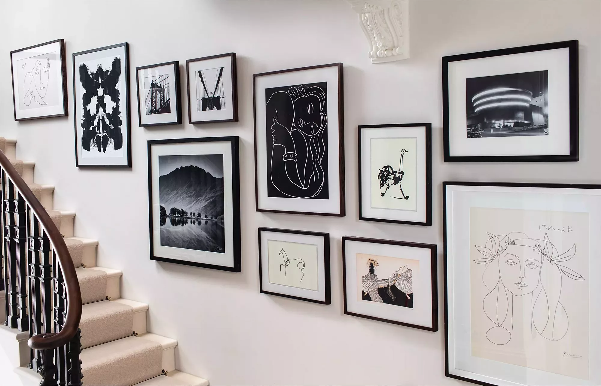 Modern staircase gallery wall with framed black-and-white art prints and sketches on a bright hallway wall