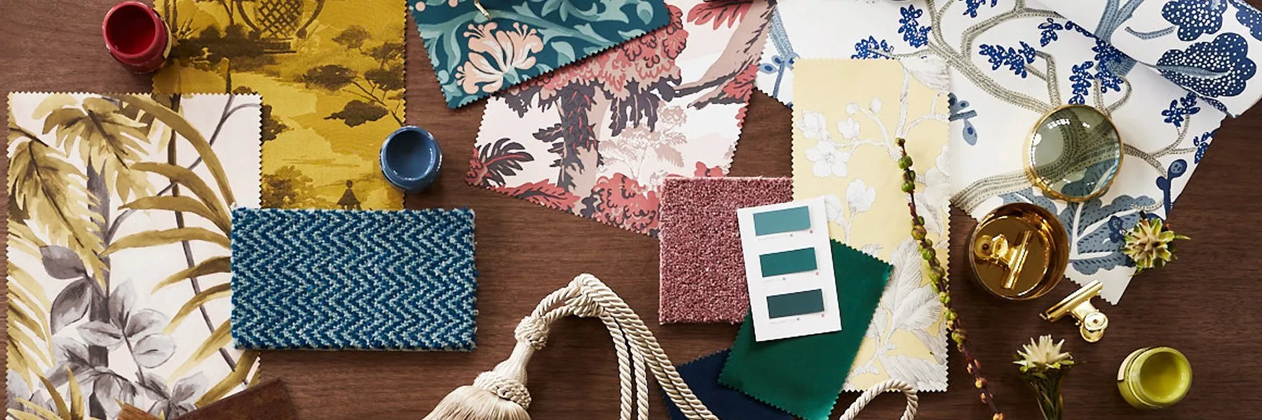 Interior design mood board with patterned fabric swatches, paint samples, rope trim and brass hardware on wooden table