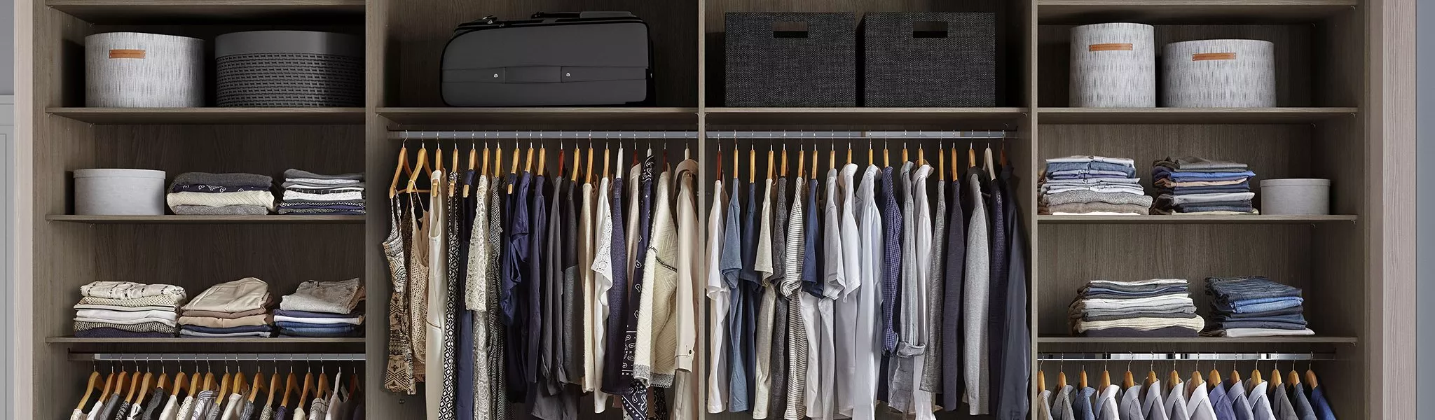 Organised wardrobe with neatly hung clothes, folded garments on shelves, and storage boxes above.