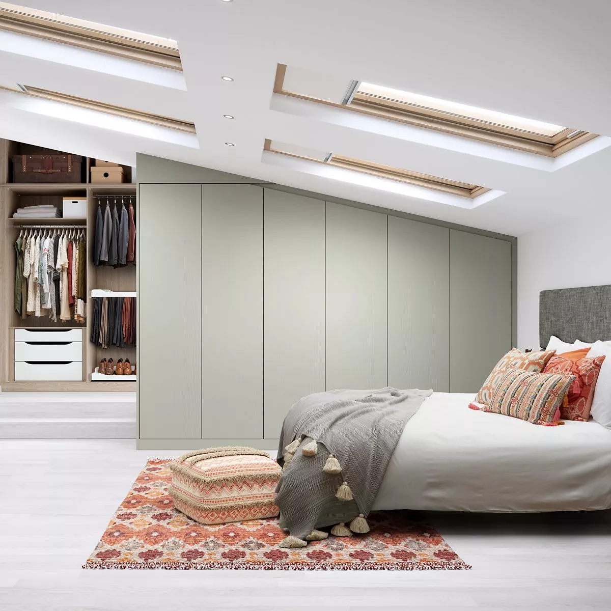 Cosy attic bedroom with skylights, fitted wardrobes, and a bed adorned with colourful cushions and a patterned rug.