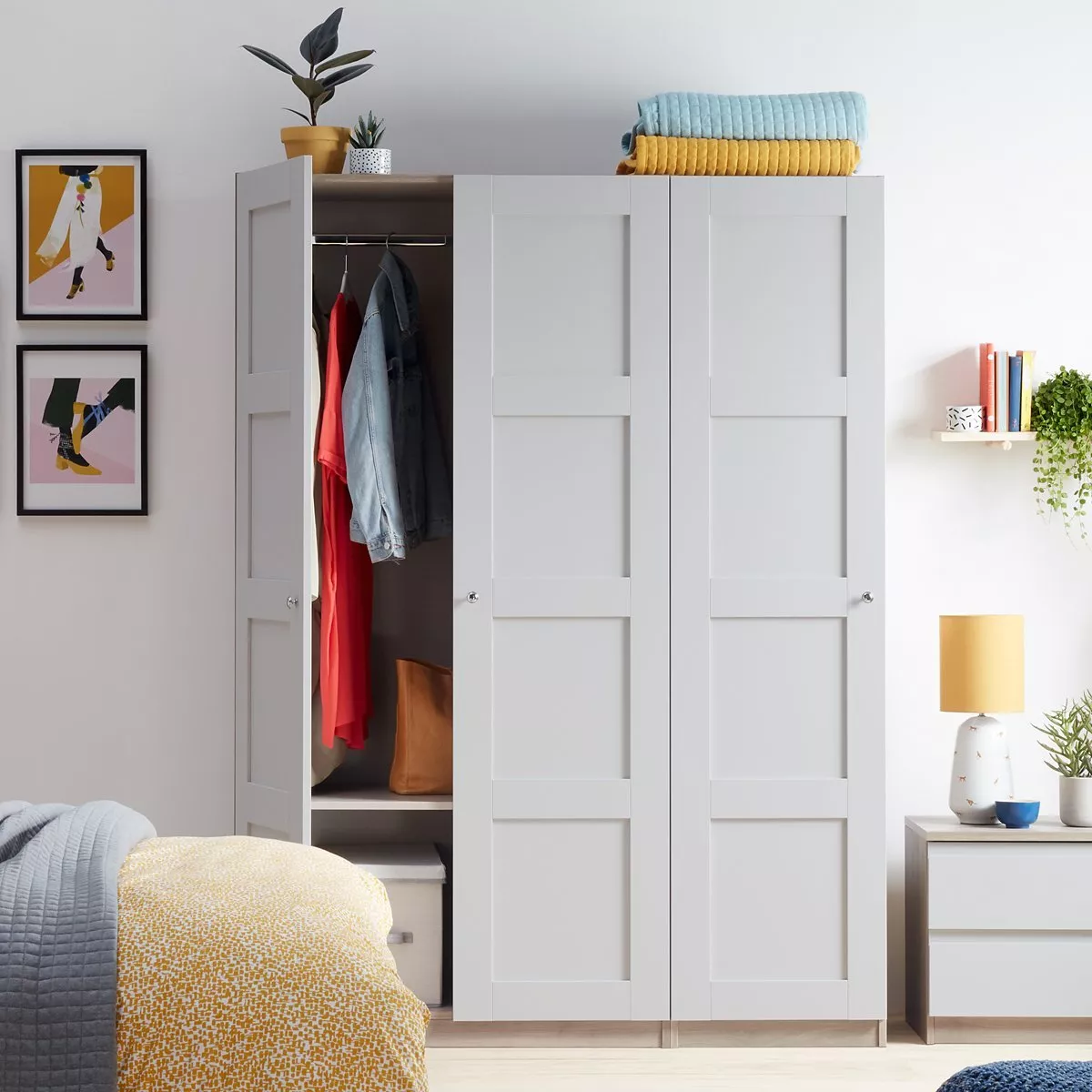Modern bedroom with a grey wardrobe, open to display clothes, and colourful decor accents on walls and furniture.