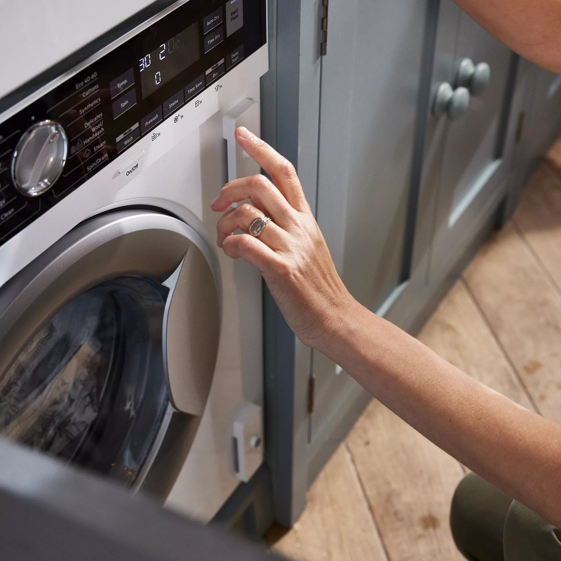 A person adjusting the settings on a modern washing machine. The control panel is illuminated.