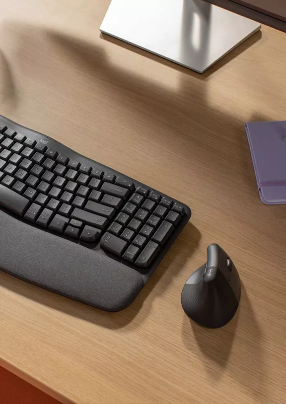 Ergonomic keyboard with wrist rest and vertical mouse on wooden desk, modern home office setup in sunlight