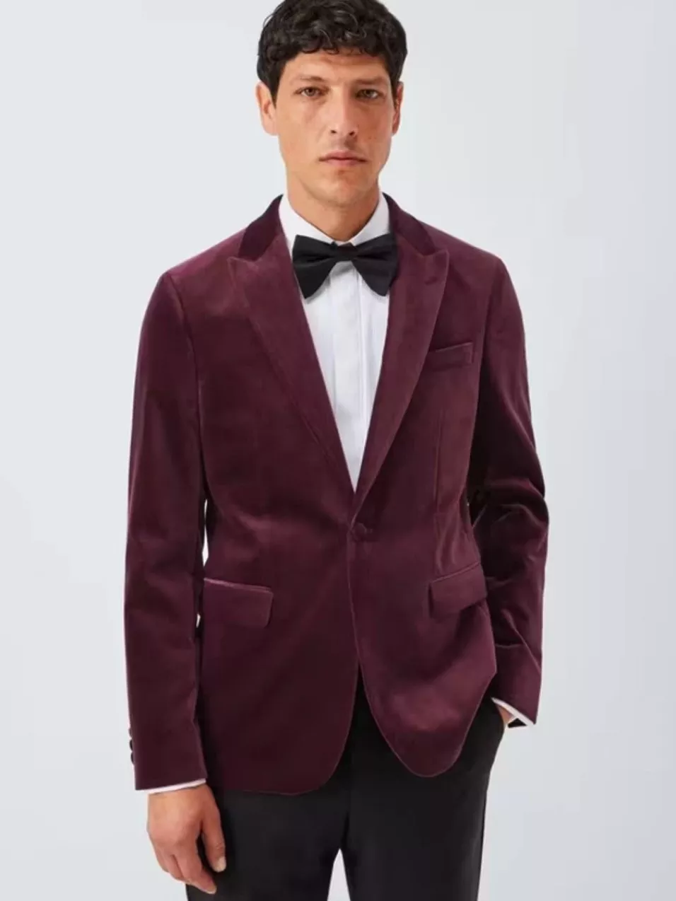 Man in a burgundy velvet tuxedo jacket, white shirt, and black bow tie, posing against a plain backdrop.