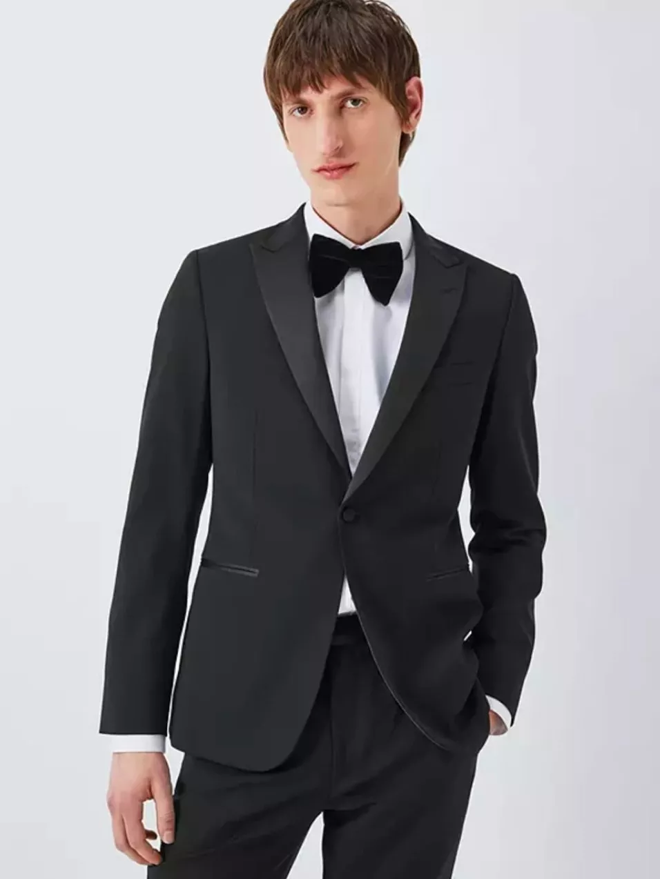 A man in a sleek black tuxedo with a white shirt and black bow tie, posing against a plain background.