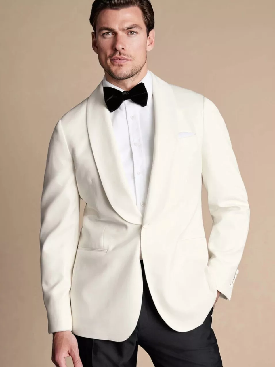 Man in a stylish white tuxedo with a black bow tie, posing confidently against a neutral background.