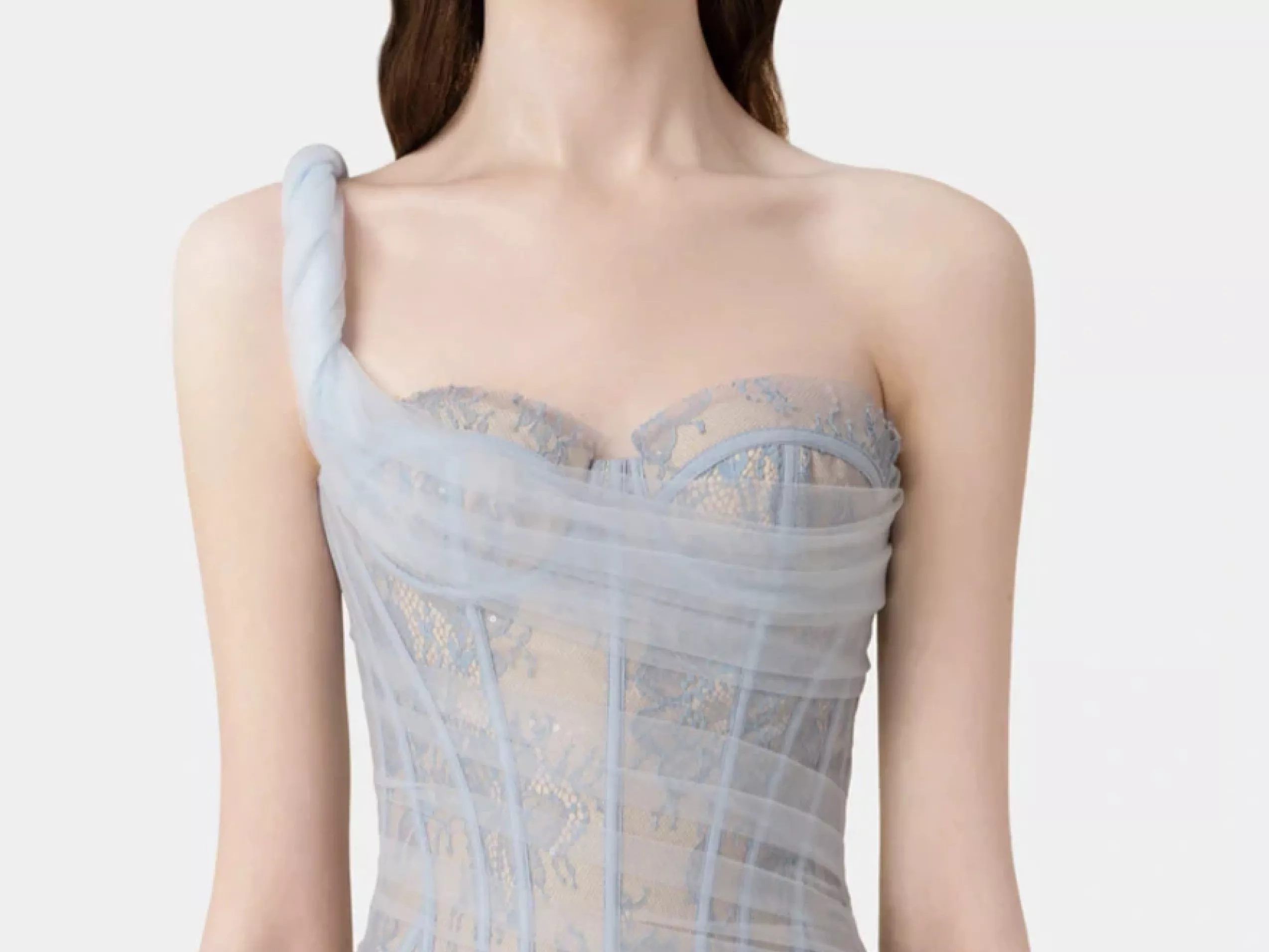 A close-up of a woman in a delicate, one-shoulder, light blue lace dress against a plain background.