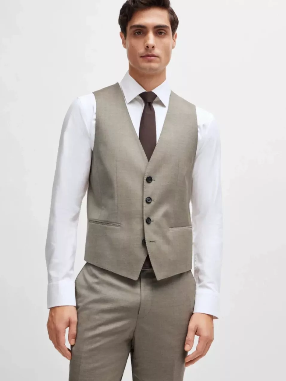 A man wearing a grey waistcoat over a white shirt with a brown tie, paired with matching trousers.