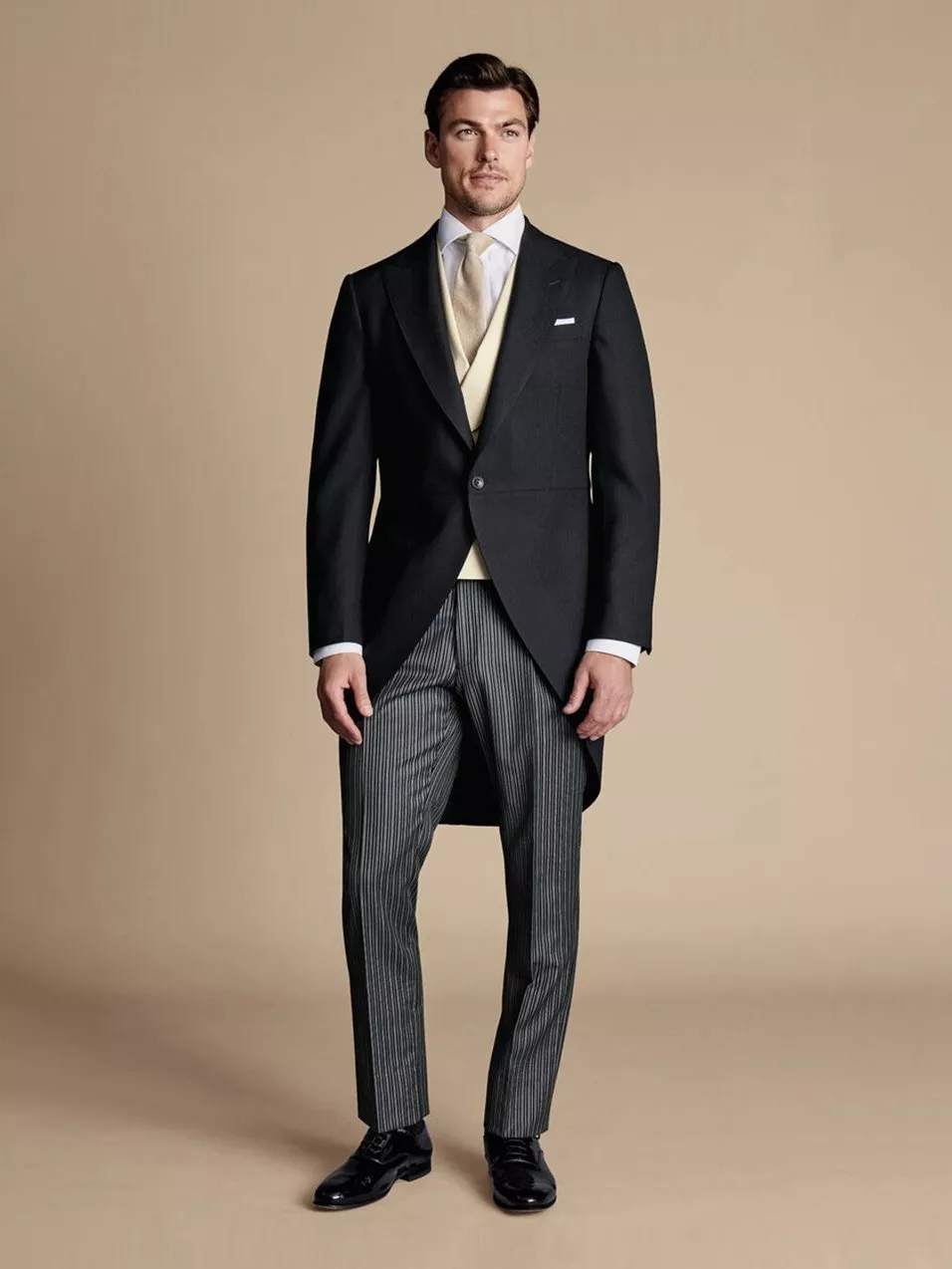 A man in formal morning dress with a black tailcoat, striped trousers, and a cream waistcoat.