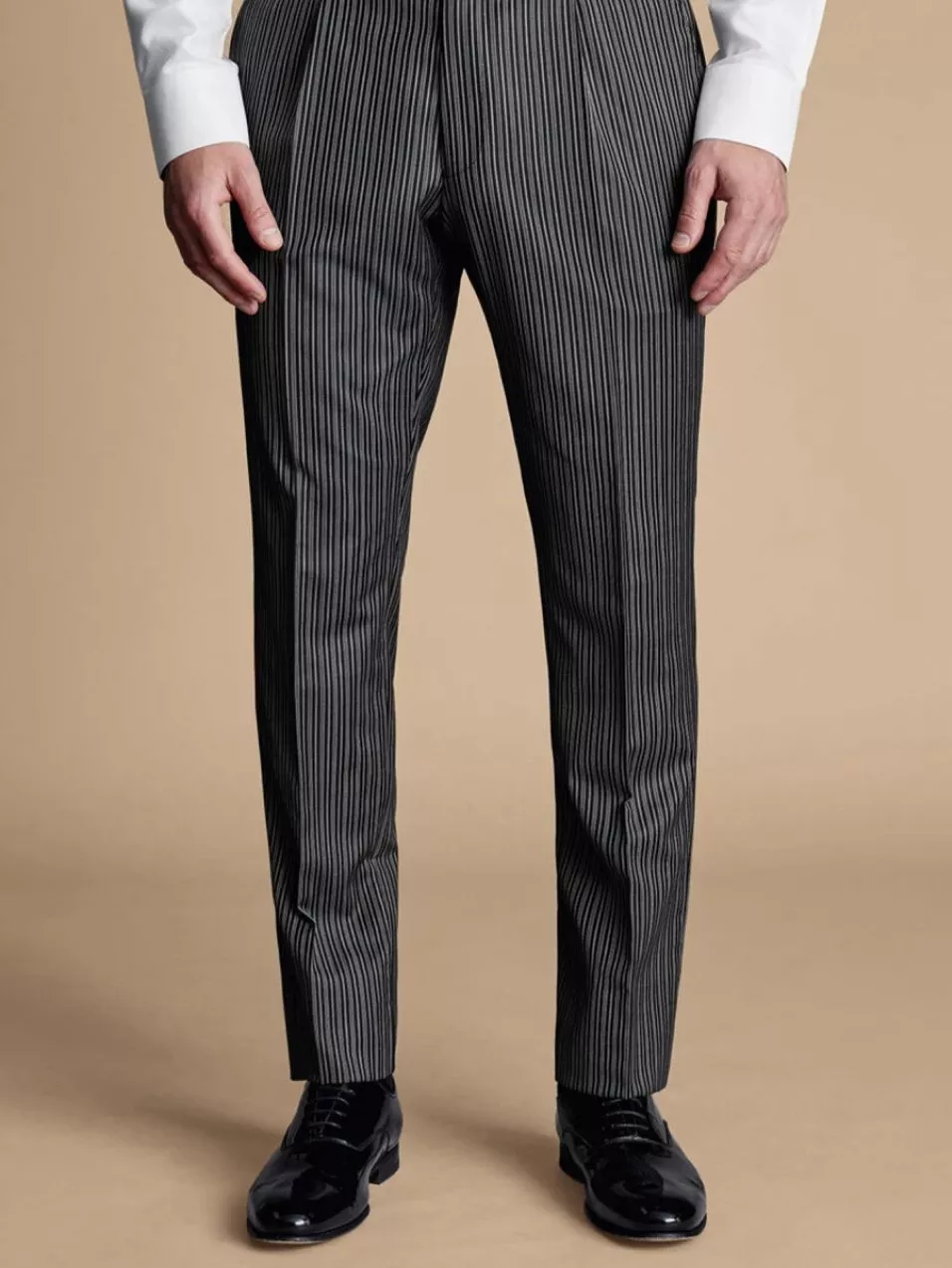 Man wearing pinstripe trousers and a white shirt, paired with black polished shoes, standing on a beige floor.