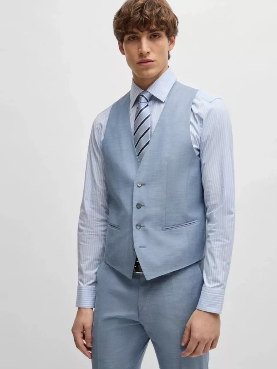 Young man in a light blue waistcoat and trousers, paired with a striped shirt and matching tie.