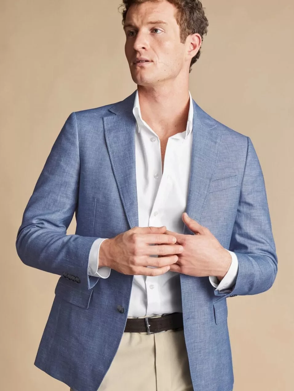A man in a light blue blazer and white shirt poses against a beige background, exuding a smart casual style.