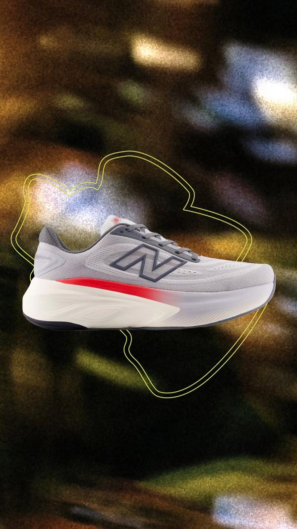 A side profile of a light grey New Balance running shoe featuring a dark blue 'N' logo and a thick, white foam midsole with a vibrant red streak.