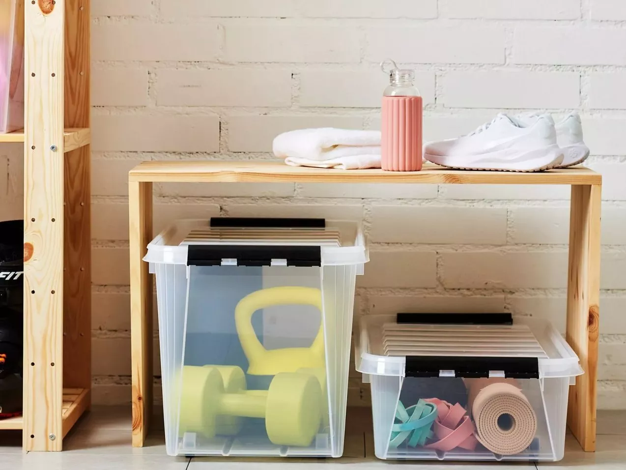 Wooden gym storage bench with towel, water bottle and trainers, plus plastic boxes with weights and mats.