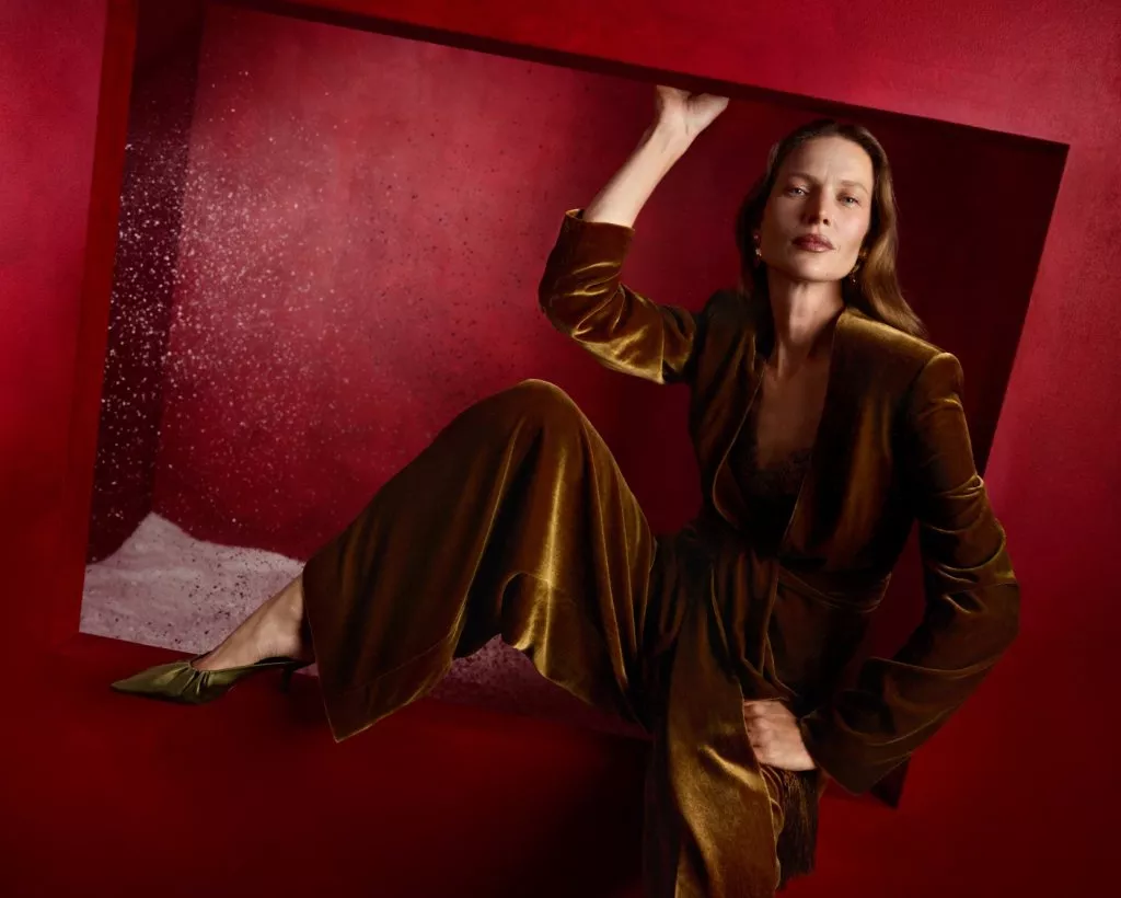 Fashion model in bronze velvet suit posing in red geometric set, editorial studio portrait with heels