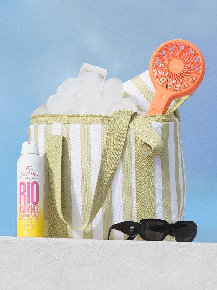 Festival essentials, including a striped cooler bag, a portable fan, and sunglasses, are on display outside