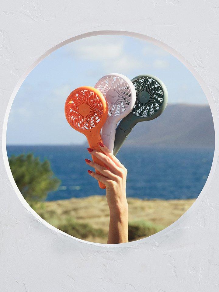 A female model's hand holding up three colourful portable handheld fans outdoors