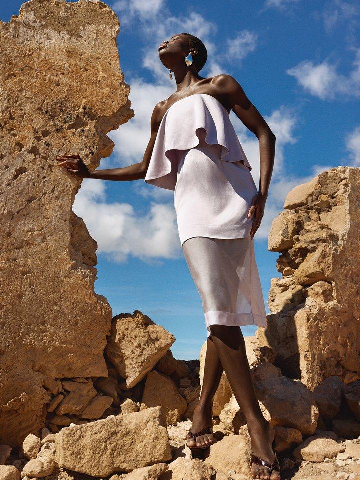Female model posing in a summery linen dress, surrounded by rocks