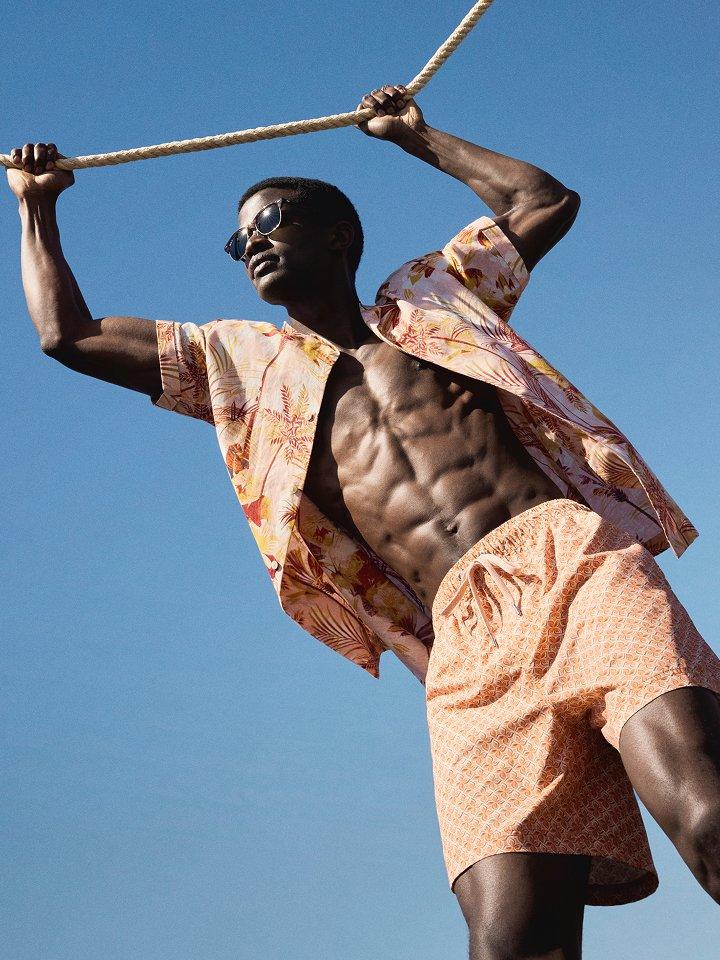 Male model holding onto a rope, wearing a summery linen shirt and shorts
