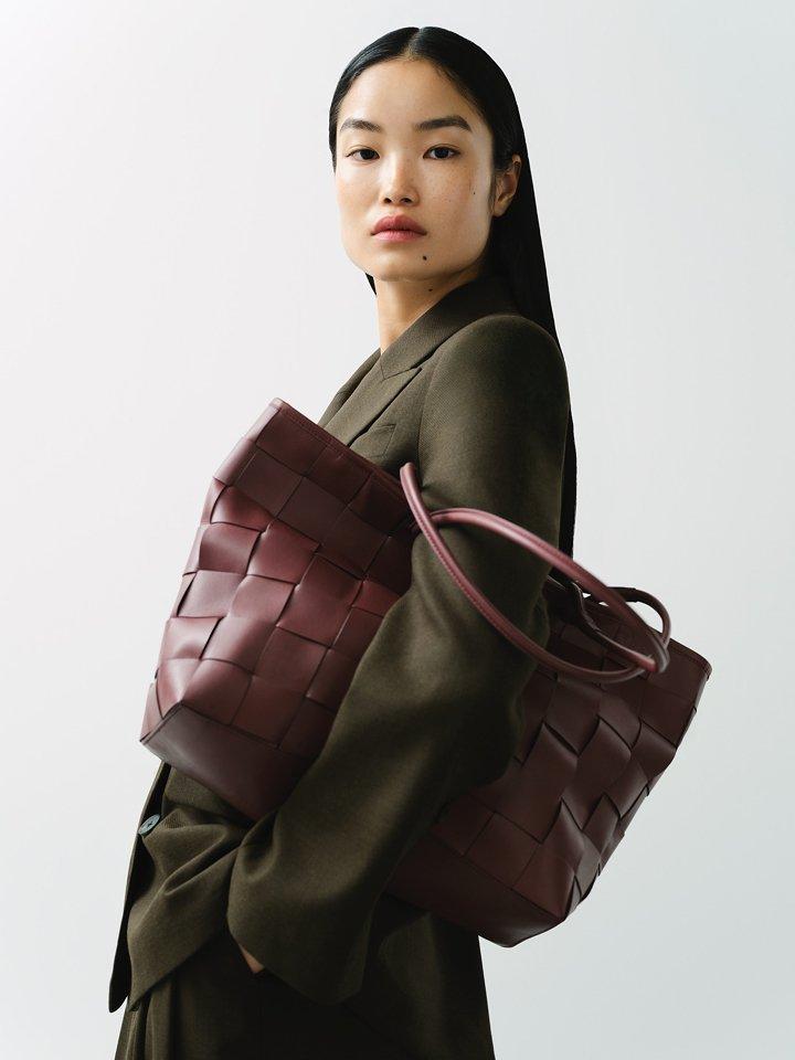 A female model posing wearing a jacket with a large burgundy coloured bag