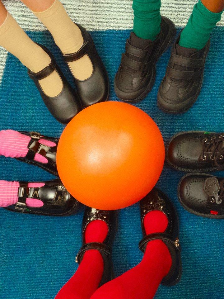 Girls' and boys' shoes with colorful socks and stockings around an orange ball