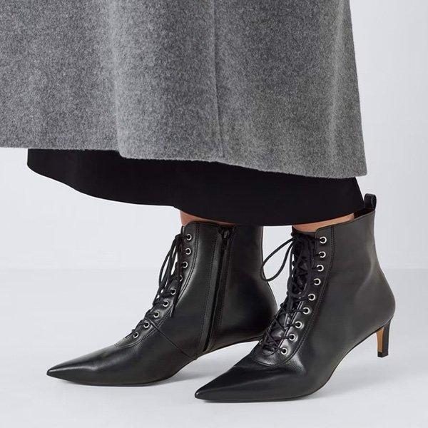 Black lace-up ankle boots with a kitten heel, worn with a black skirt and grey coat.