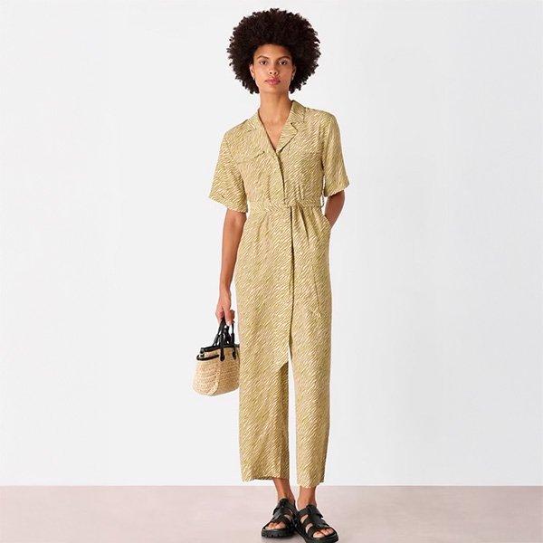 Woman in patterned jumpsuit holding a straw bag.