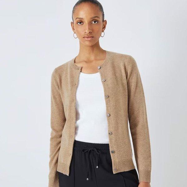 A woman wears a classic, long-sleeved, beige knit cardigan with a round neckline and small buttons, over a white top and black pants.