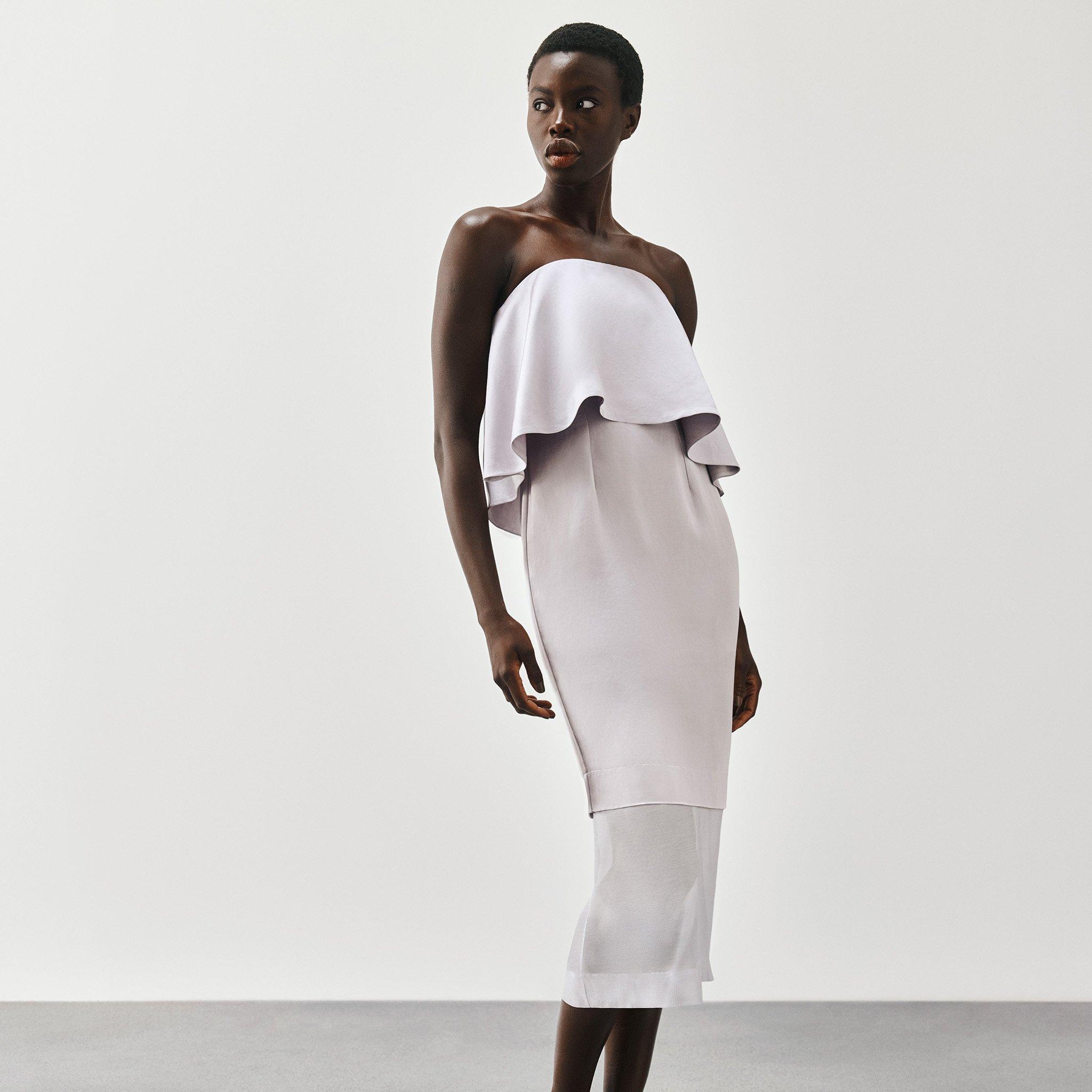 A woman wearing a strapless, layered white dress, standing against a plain light background.