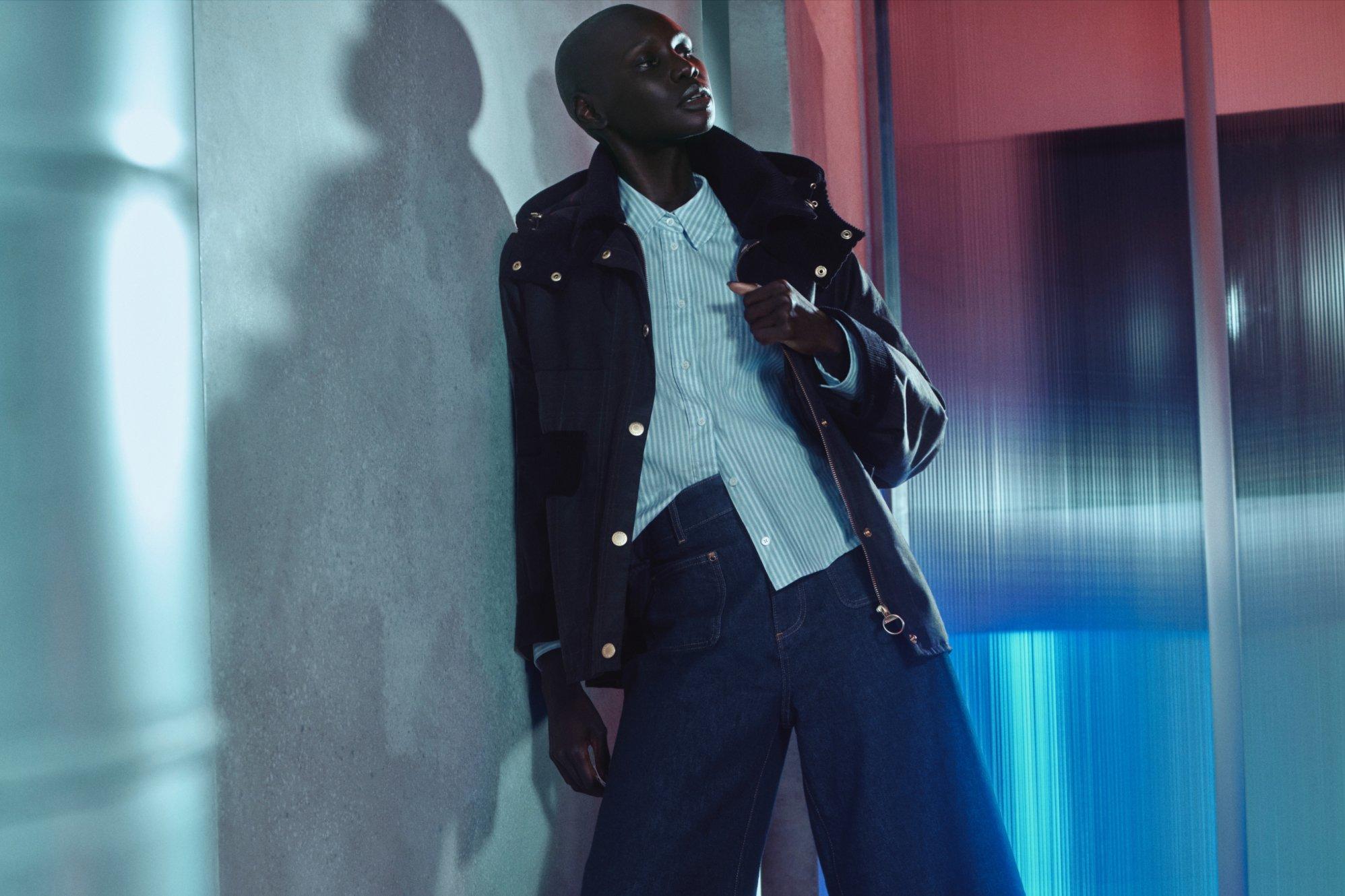 women leaning against a conrete wall with stripey shirt and denim and smart jacket