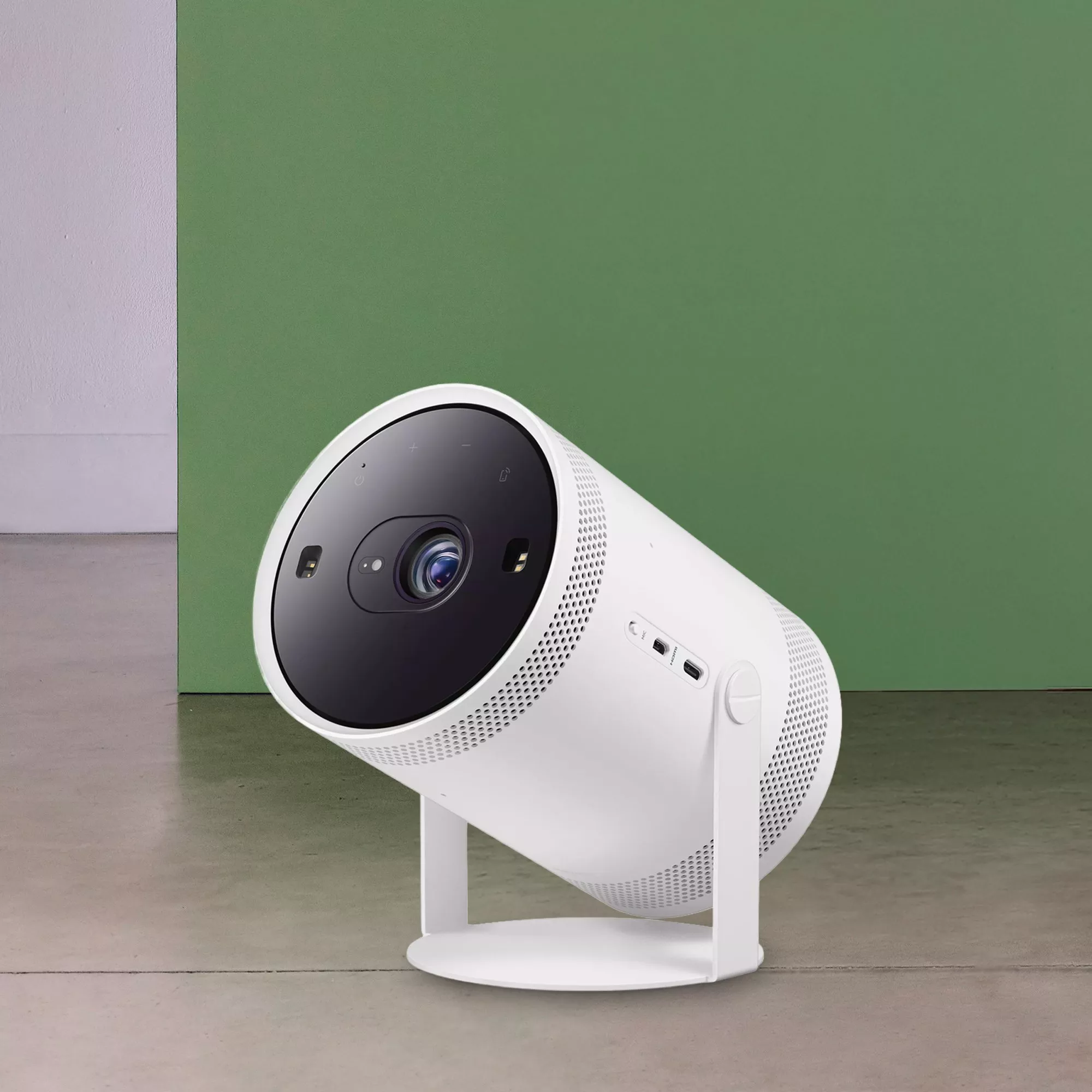 Modern white portable smart projector on stand, close-up lens view against green wall for home cinema setup