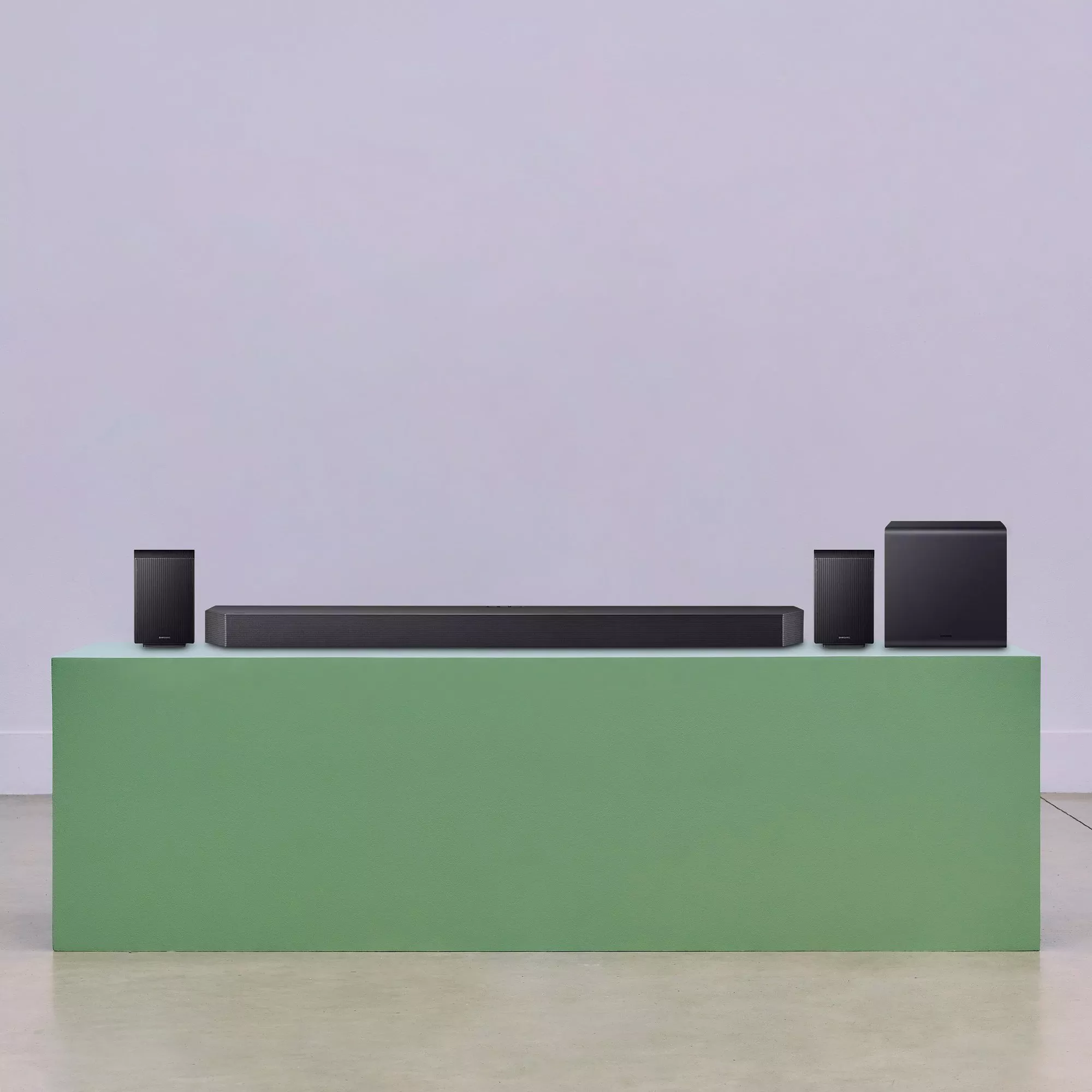 Soundbar home cinema speaker system with subwoofer and rear speakers on green stand, studio backdrop