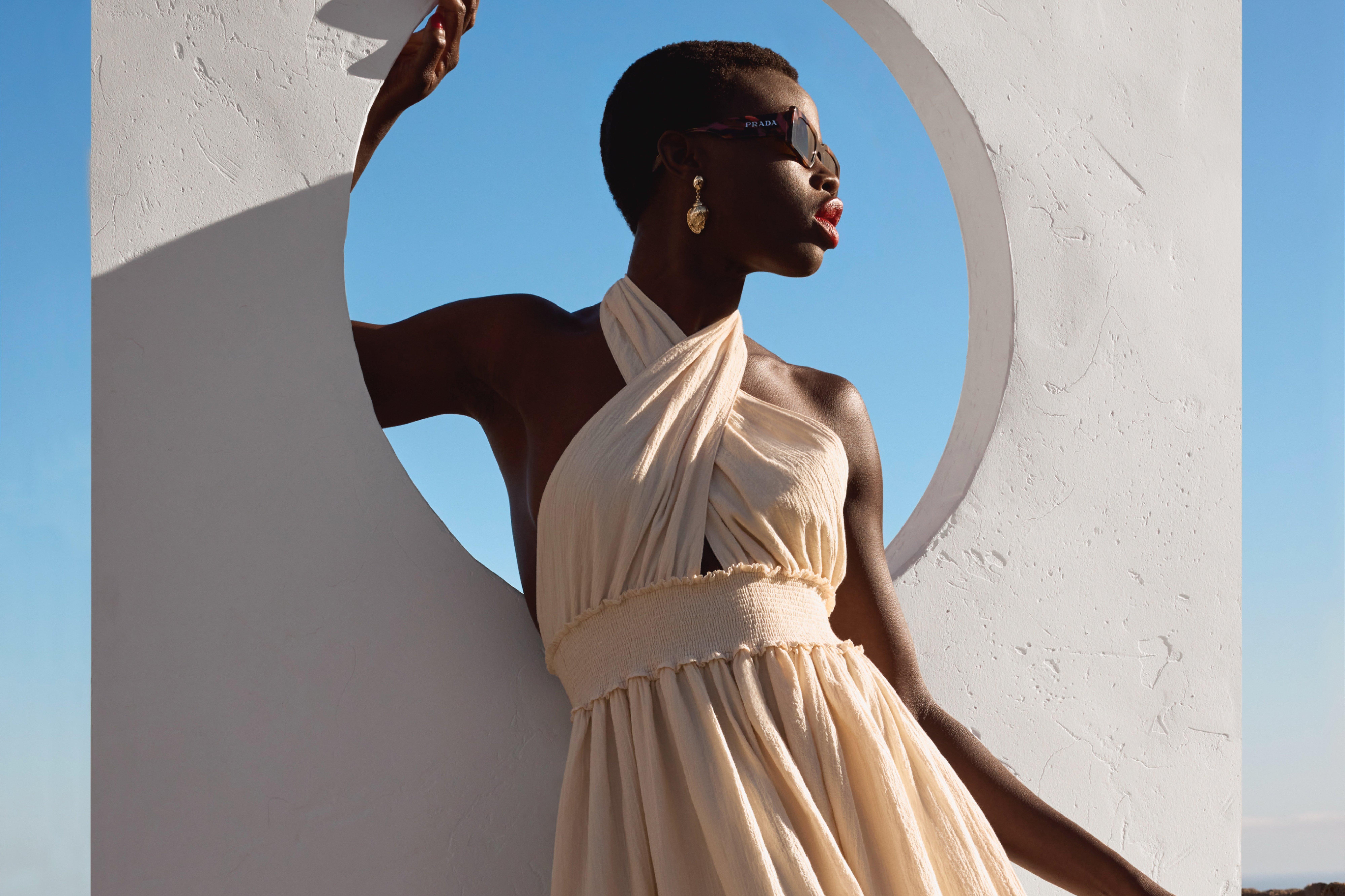 women in a off white long maxi dress leaning in a window in a white wall
