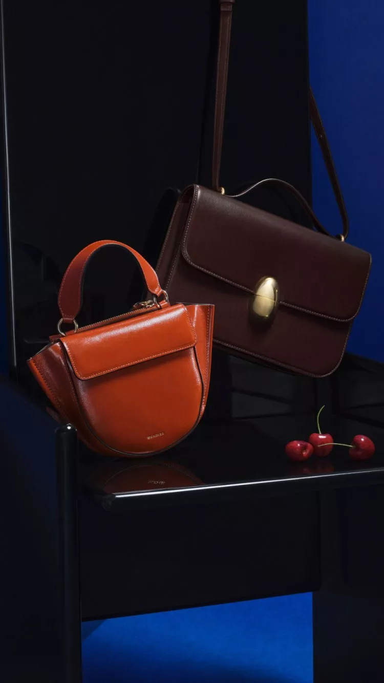 Luxury leather handbags in brown and tan on a chair with cherries, elegant fashion accessories still life