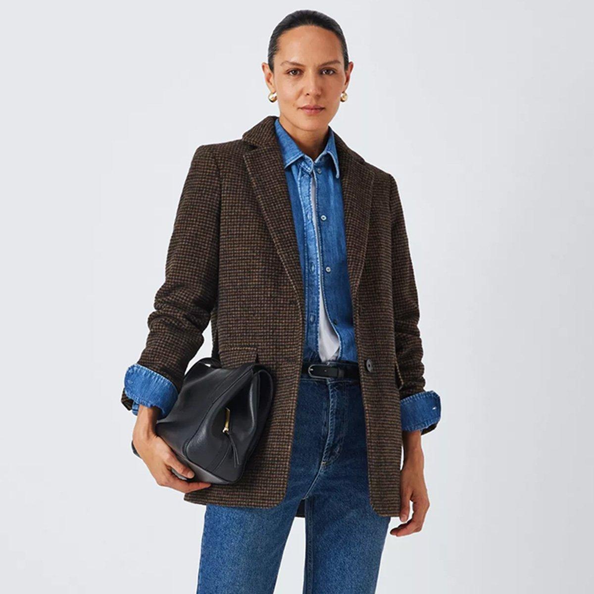 Woman in brown jacket, and jean shirt, holding black leather bag by her side.