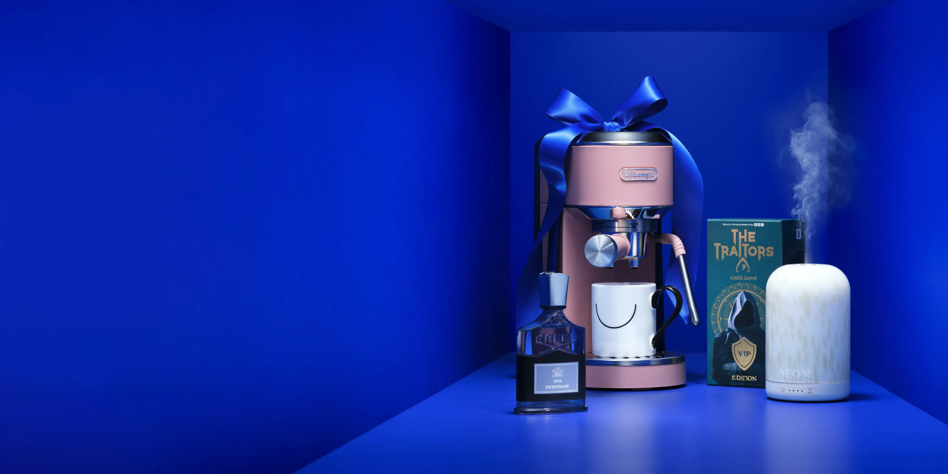 Luxury gift set with espresso machine, perfume, mug, card game and NEOM diffuser on blue background
