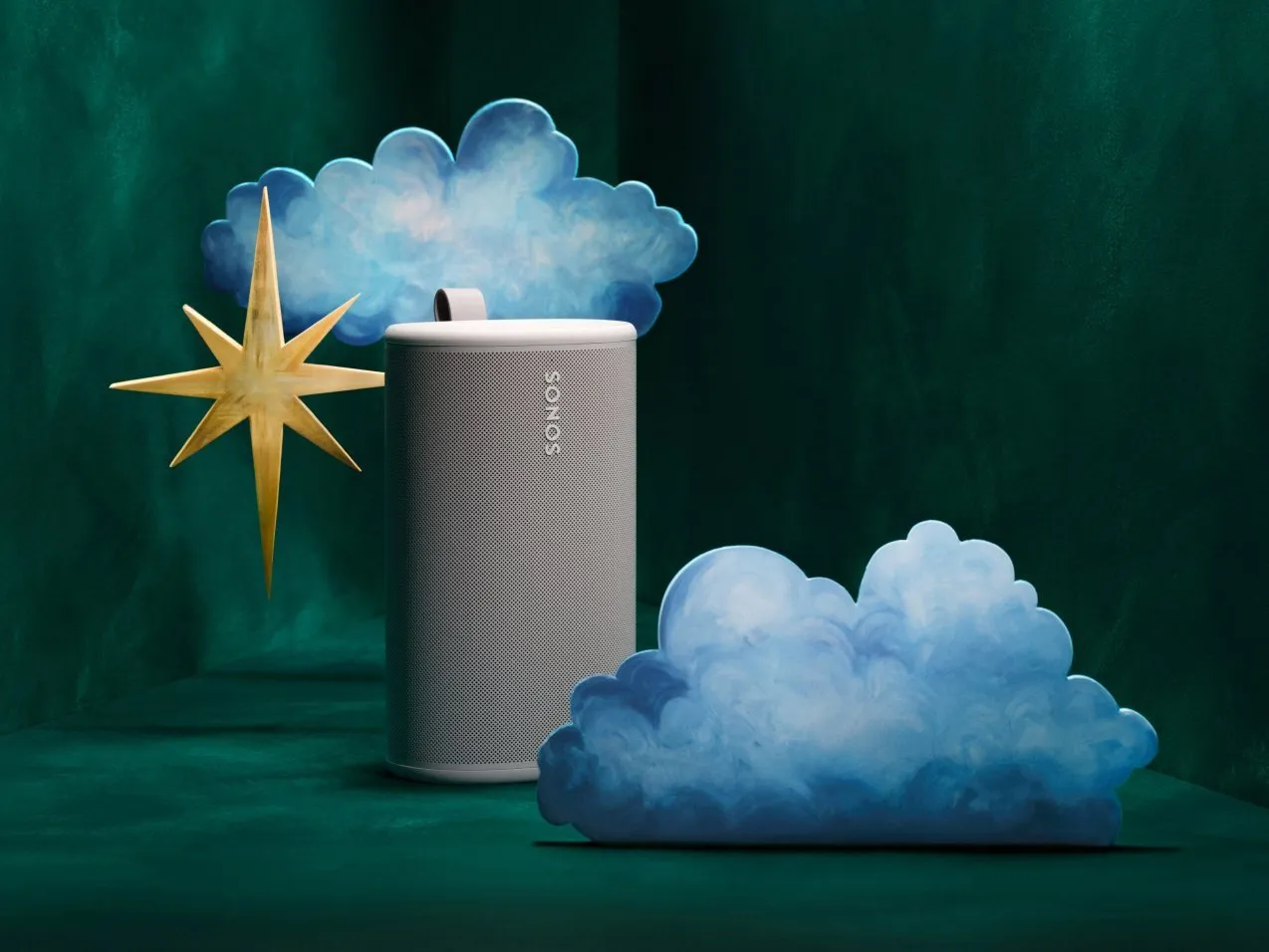Sonos portable smart speaker in white, styled with blue clouds and a gold star on a dark green backdrop