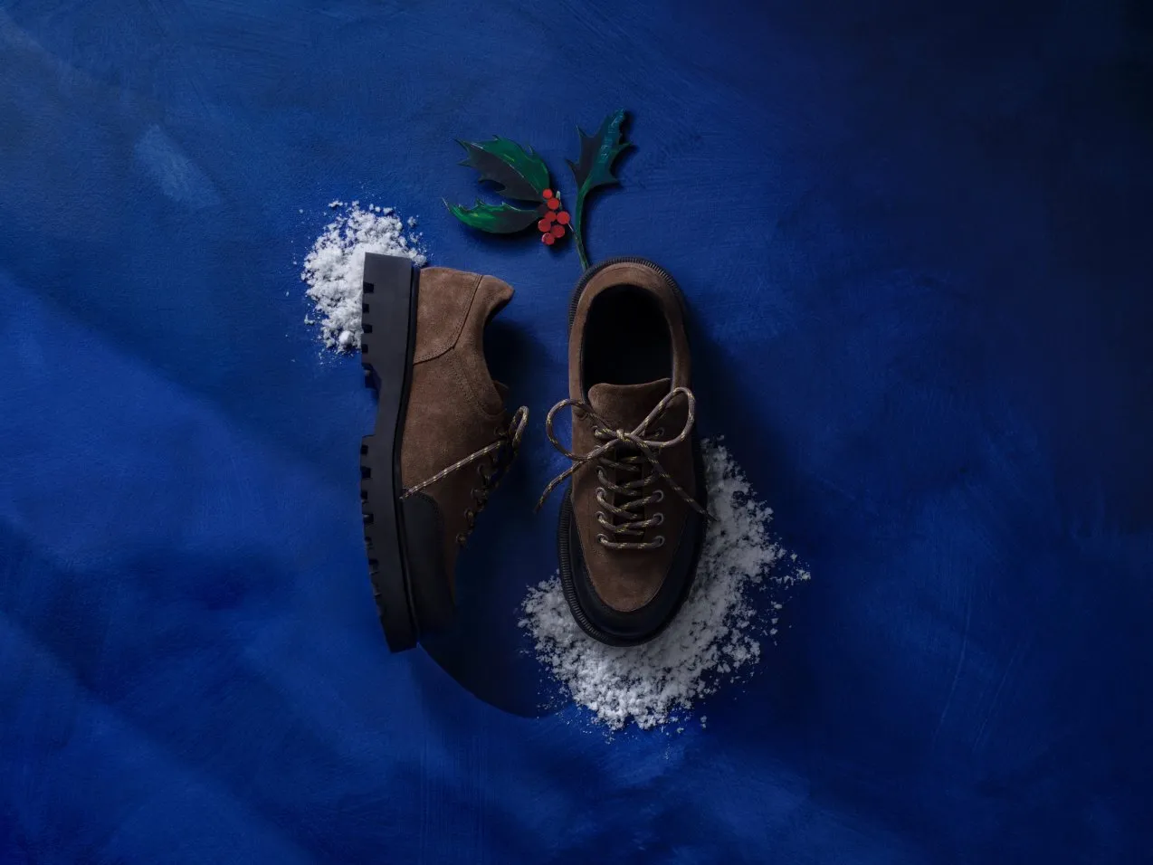 Brown suede lace-up shoes on blue background with faux snow and holly, winter footwear product photo