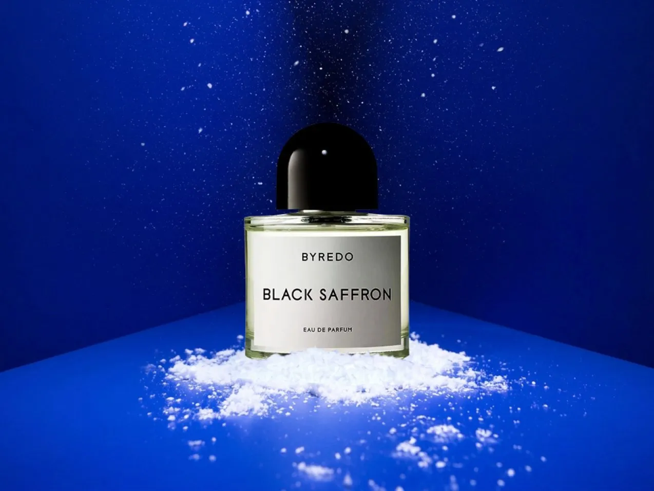 Byredo Black Saffron eau de parfum bottle on blue backdrop with scattered white powder and mist effect