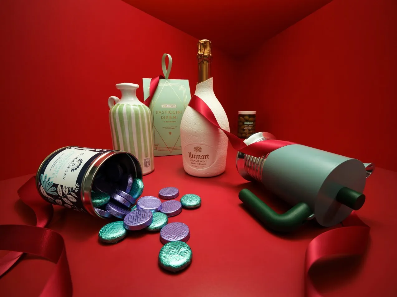 Festive luxury gift set with champagne bottle, chocolates, ribbon, and tins on red background still life